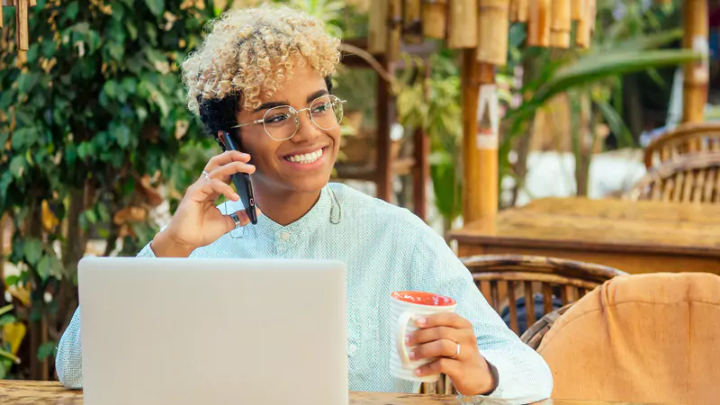Smiling nurse working remotely, using laptop and phone, embracing flexibility of online nursing jobs