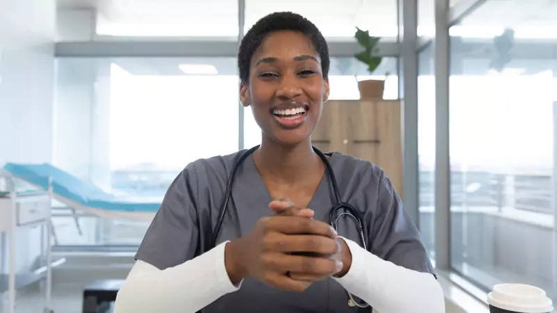 Smiling remote nurse in scrubs confidently sitting at a desk, highlighting the importance of finding the right online nursing job fit