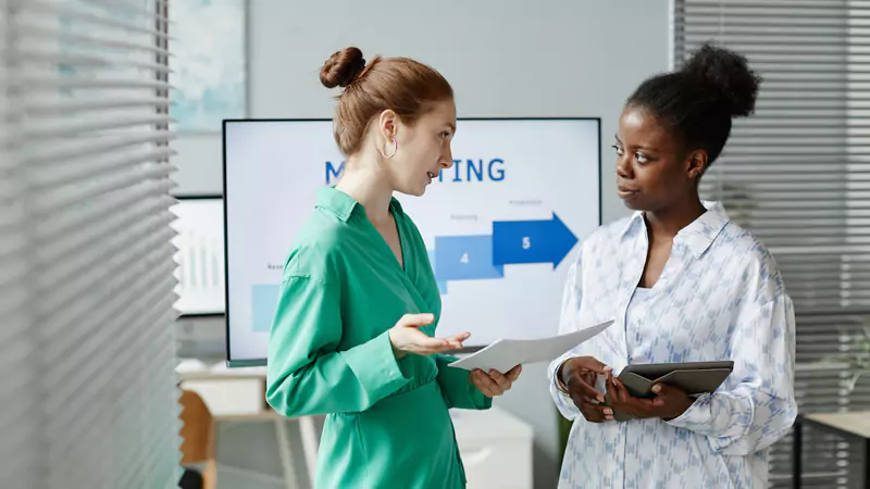 Two female colleagues discussing core components of travel nurse pay during a meeting