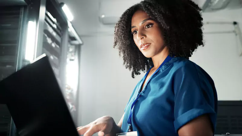 Informatics nurse using a laptop in a server room, illustrating the integration of nursing informatics with technology and data management