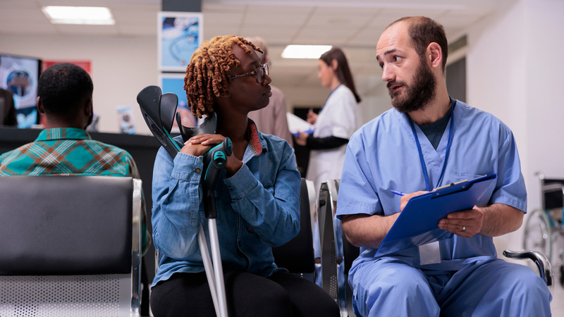 Healthcare worker consulting a female patient with crutches in hospital waiting area