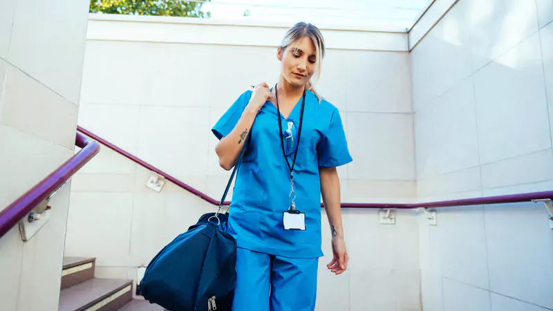 Travel nurse in blue scrubs walking down stairs after completing shift, symbolizing financial success and career freedom
