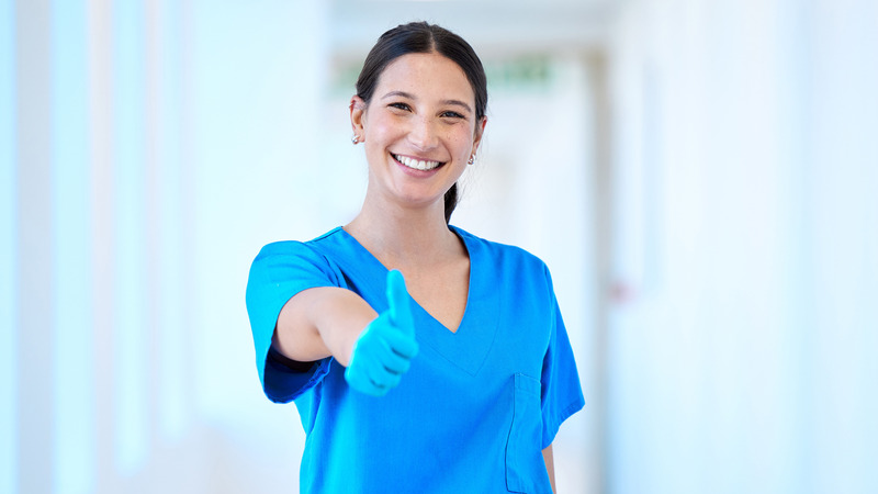 Smiling female healthcare worker in scrubs giving a thumbs-up gesture