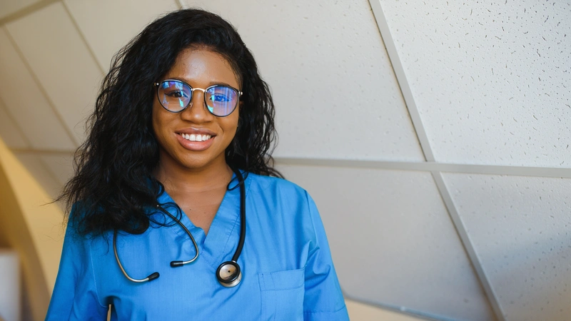 Confident female nurse in blue scrubs and glasses smiling, representing the first steps toward a career in aesthetic cosmetic nursing