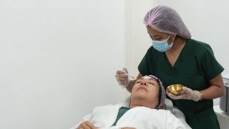 Aesthetic cosmetic nurse applying treatment to a female client’s face during a skincare procedure in a clinical spa setting