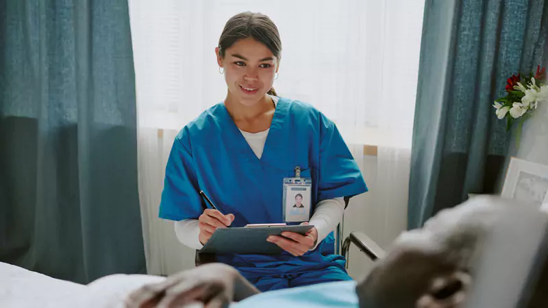 nurse-navigator-smiling-while-taking-notes-with-elderly-patient