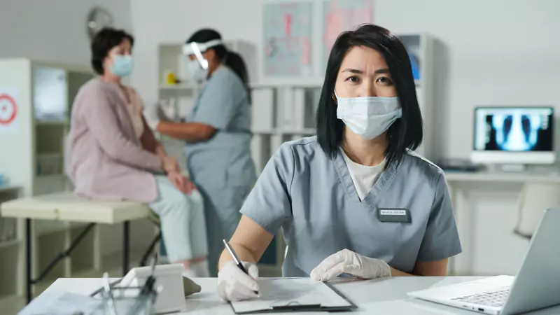 female-healthcare-worker-in-scrubs-writing-on-clipboard-in-exam-room